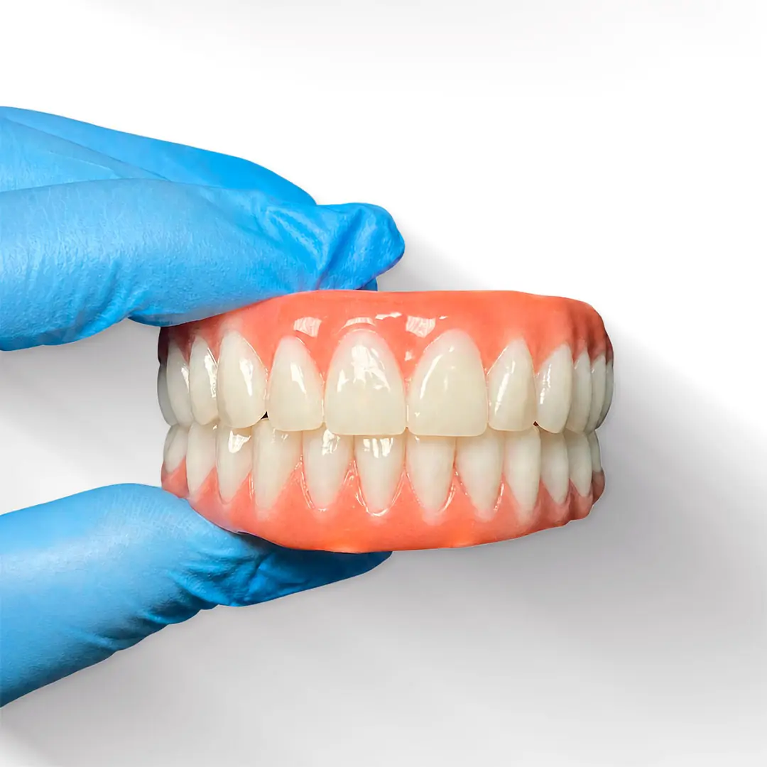Prótese dentária completa segurada por mãos com luvas clínicas